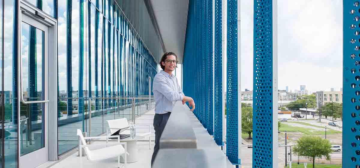Man standing on balcony of a blue and white office building (Tier 1_Office_Houston_AML_4462)
