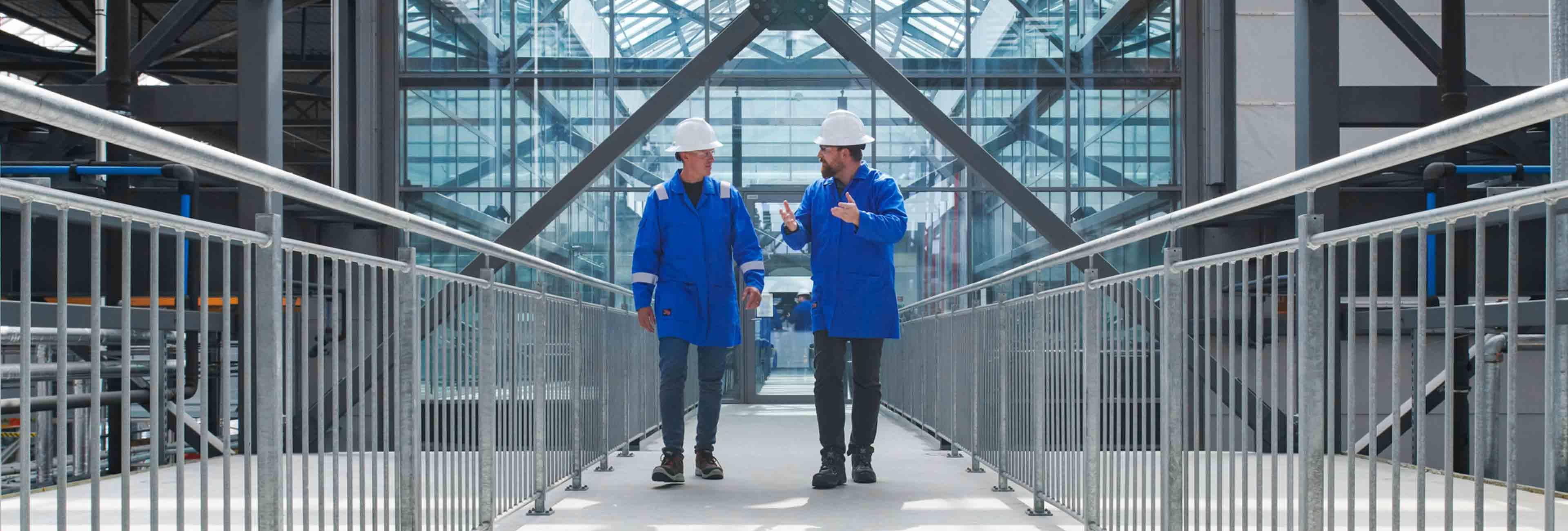两名穿着蓝色实验室工作服的欧洲杯投注平台员工在走廊上互相交谈