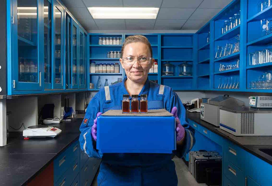 穿着蓝色工作服的妇女在实验室里拿着溶剂样品的照片。